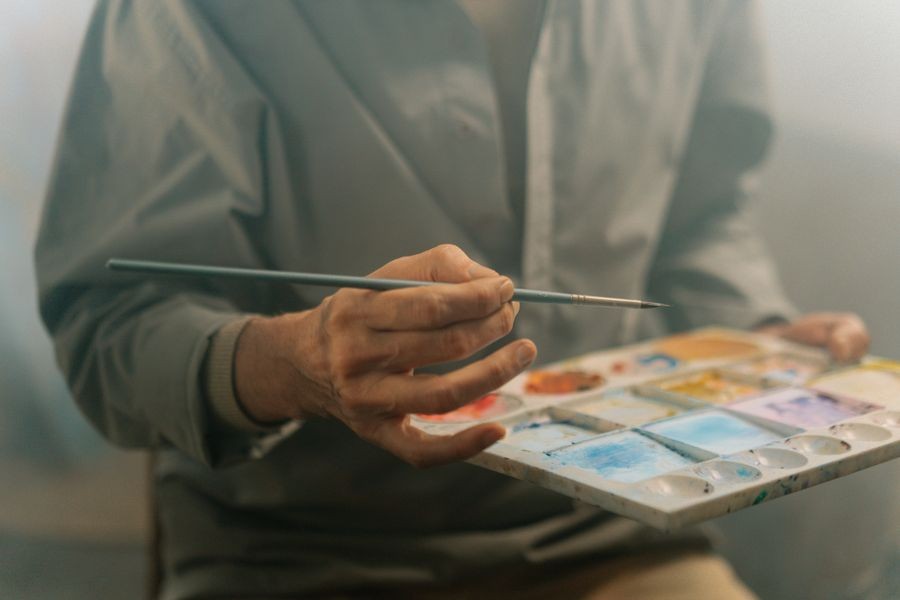 Close-up of an artist's hand holding a paintbrush and a palette of watercolours
